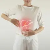Kobieta wskazuje rękami na okolice brzucha, gdzie widoczna jest narysowana, podświetlona na czerwono wątroba.