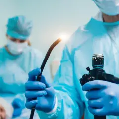 Lekarz w niebieskim fartuchu i rękawiczkach trzyma endoskop. To narzędzie do badania wnętrza ciała, czyli endoskopia co to jest.