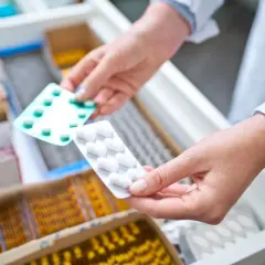 Farmaceuta wybiera opakowanie tabletek, być może zawierających doloxib, z szuflady aptecznej.