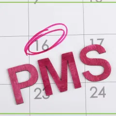 Drewniane litery PMS na kalendarzu, dzień 16 zaznaczony różowym kółkiem.