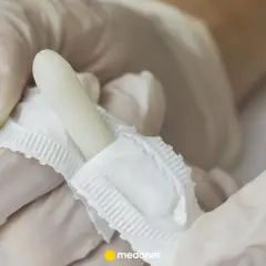 Rękawiczki medyczne trzymają biały czopek, prawdopodobnie torecan, gotowy do użycia.