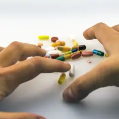 Dłonie sięgają po garść kolorowych tabletek i kapsułek, wśród których widać lek tegretol.