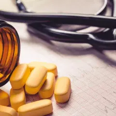 Lekarz przepisuje cyprofloksacynę. Tabletki wypadają z brązowej butelki na papier EKG, obok leży stetoskop.