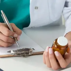 Lekarz przepisuje receptę na kolchicynę, trzymając buteleczkę z lekami.