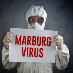 Osoba w kombinezonie ochronnym trzyma tabliczkę z napisem "MARBURG VIRUS".