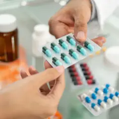 Farmaceuta podaje pacjentowi blistry z lekami, w tym z niebiesko-zielonymi kapsułkami edolox.