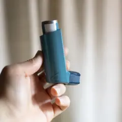 Dłoń trzyma niebieski inhalator z salbutamolem, gotowy do ulgi w astmie.
