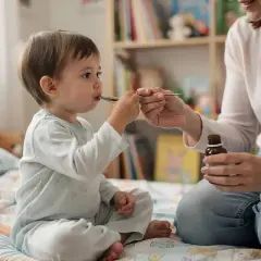 Mama podaje dziecku syrop na łyżeczce. Maluch dzielnie przyjmuje lek, być może to Tussipect na kaszel.