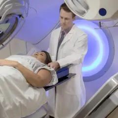 Pacjentka leży na stole zabiegowym, a lekarz nadzoruje przebieg radioterapii.