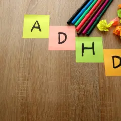 Kolorowe karteczki z literami A, D, H, D układają się w słowo "ADHD". Obok leżą pisaki i pomięte kartki.