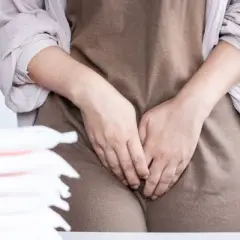 Stos podpasek obok kobiety, która zakrywa dłoniemi okolice intymne. Zapewnienie komfortu i higieny, jak w przypadku izovag.