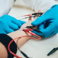 Lekarz w niebieskich rękawiczkach podłącza elektrody do ręki pacjenta podczas badania EMG.
