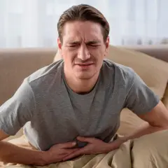 Mężczyzna w łóżku trzymający się za brzuch z wyrazem bólu na twarzy.