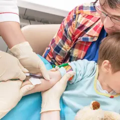 Pielęgniarka pobiera krew od dziecka, które trzyma ojciec.