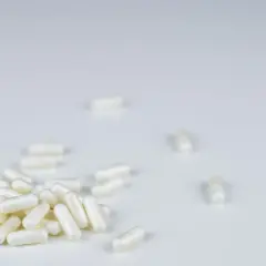 Białe kapsułki leku Anapran rozsypane na białym tle.