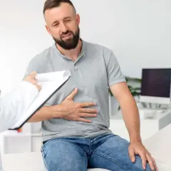 Mężczyzna z bólem brzucha, prawdopodobnie jelitówka, rozmawia z lekarką w gabinecie.