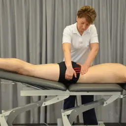 Fizjoterapeuta wykonuje masaż okolicy stawu krzyżowo biodrowego pacjenta leżącego na kozetce.