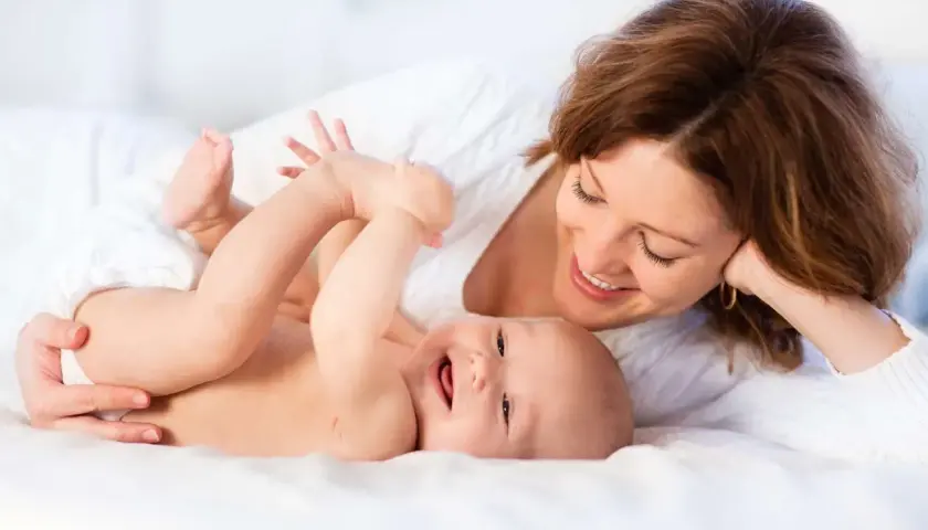Uśmiechnięta mama patrzy na radosne dziecko leżące na białym tle.
