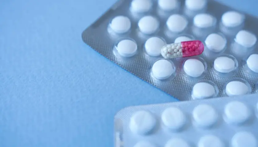 Dwie blistry białych tabletek, jedna z nich zawiera kapsułkę z różowymi granulkami, przypominającą clonazepam.
