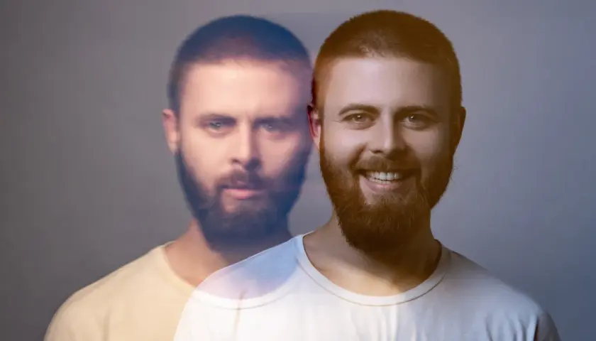 Dwóch mężczyzn z brodami, jeden uśmiechnięty, drugi z poważnym wyrazem twarzy, na szarym tle.