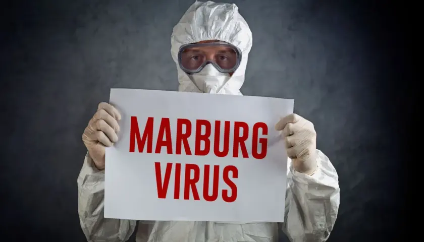 Osoba w kombinezonie ochronnym trzyma tabliczkę z napisem "MARBURG VIRUS".