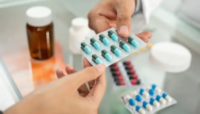 Farmaceuta podaje pacjentowi blistry z lekami, w tym z niebiesko-zielonymi kapsułkami edolox.