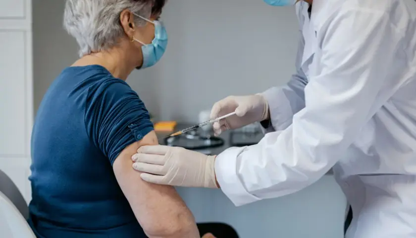 Starsza pani otrzymuje szczepionkę na covid. Lekarz w białym fartuchu i rękawiczkach podaje zastrzyk.