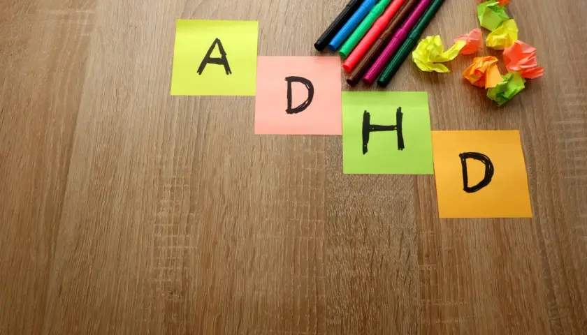 Kolorowe karteczki z literami A, D, H, D układają się w słowo "ADHD". Obok leżą pisaki i pomięte kartki.