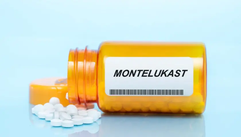 Pomarańczowa buteleczka z lekami na astmę, z napisem MONTELUKAST i rozsypanymi tabletkami.