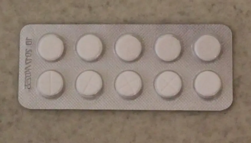 Opakowanie z dziesięcioma białymi tabletkami, niektóre z nacięciem. Może to być lek na receptę, np. tizagelan.