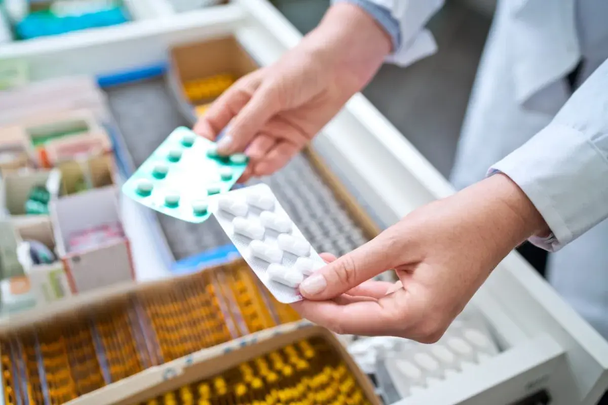 Farmaceuta wybiera opakowanie tabletek, być może zawierających doloxib, z szuflady aptecznej.