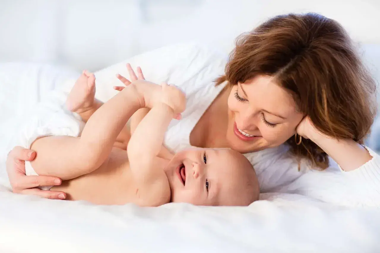 Uśmiechnięta mama patrzy na radosne dziecko leżące na białym tle.