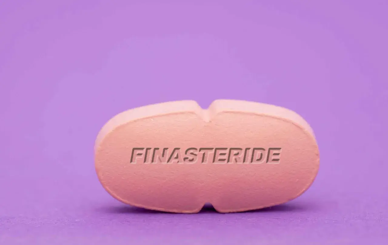 Różowa tabletka z napisem FINASTERIDE na fioletowym tle.