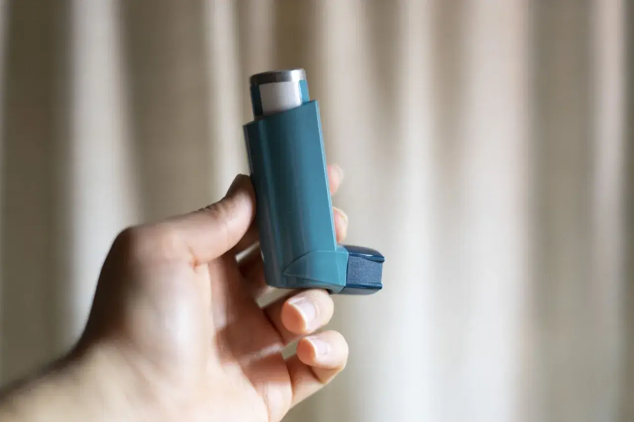 Dłoń trzyma niebieski inhalator z salbutamolem, gotowy do ulgi w astmie.