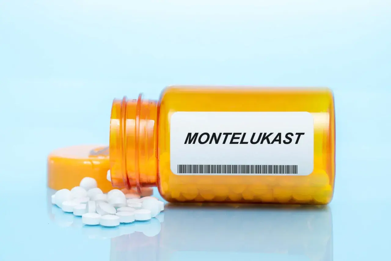Pomarańczowa buteleczka z lekami na astmę, z napisem MONTELUKAST i rozsypanymi tabletkami.