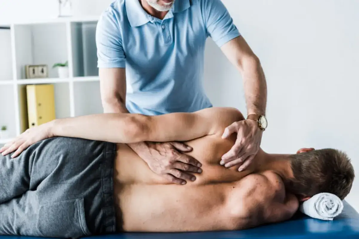 Fizjoterapeuta masuje plecy pacjenta, łagodząc ból kręgosłupa lędźwiowego.
