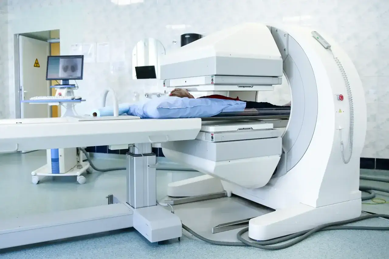 Pacjent leży na stole aparatu do scyntygrafii. Urządzenie otacza pacjenta, wykonując badanie diagnostyczne.